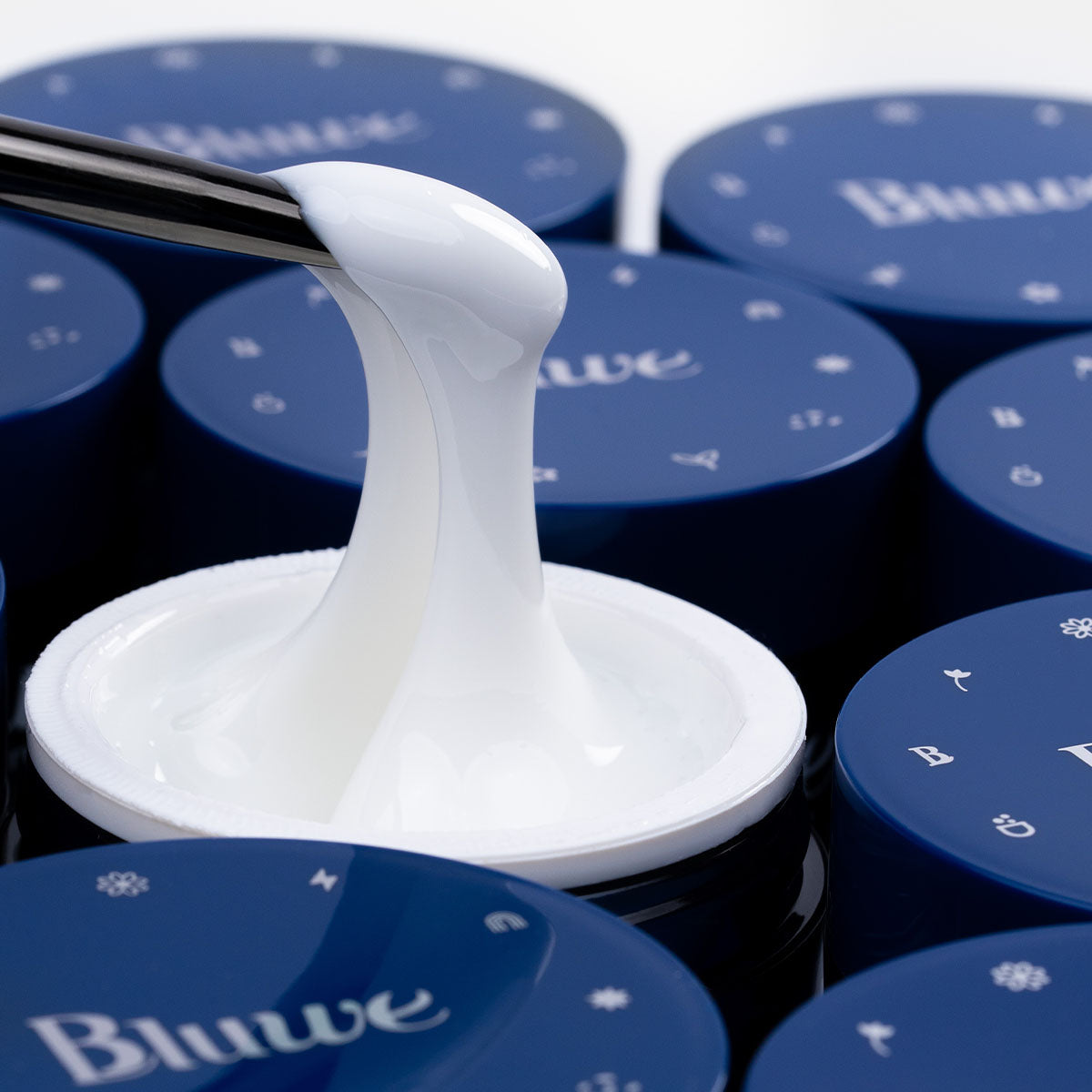 a foto é composta por vários potes de gel, o foco principal está em um pote de gel construtor branco baby, de cor branca. o gel está sendo manipulado com um pincel