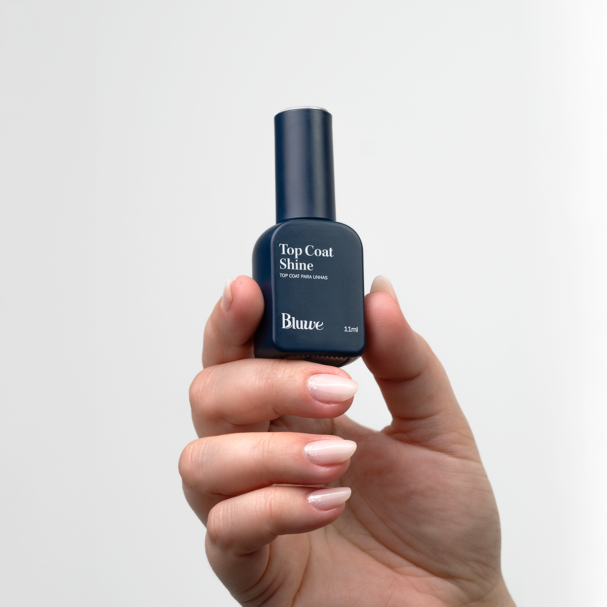Uma mão segurando o produto Top Coat Shine da marca Bluwe