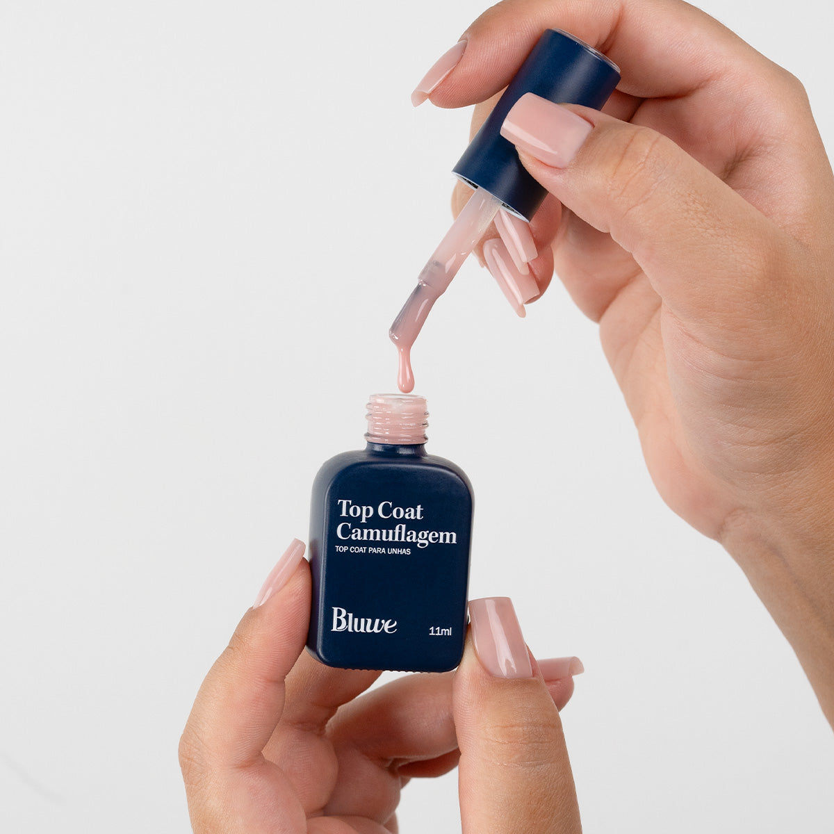 Produto Top Coat Camuflagem da marca Bluwe. Duas mãos segurando e manipulando o vidro em formato de esmalte