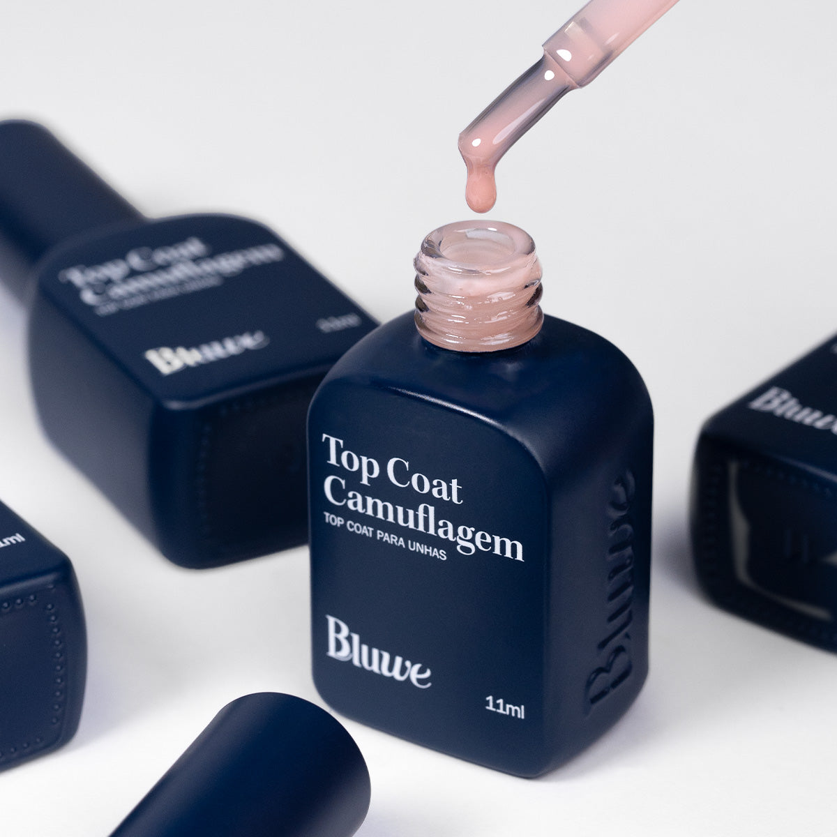 Frascos do Top Coat Camuflagem em fundo branco e um em primeiro plano sendo manipulado